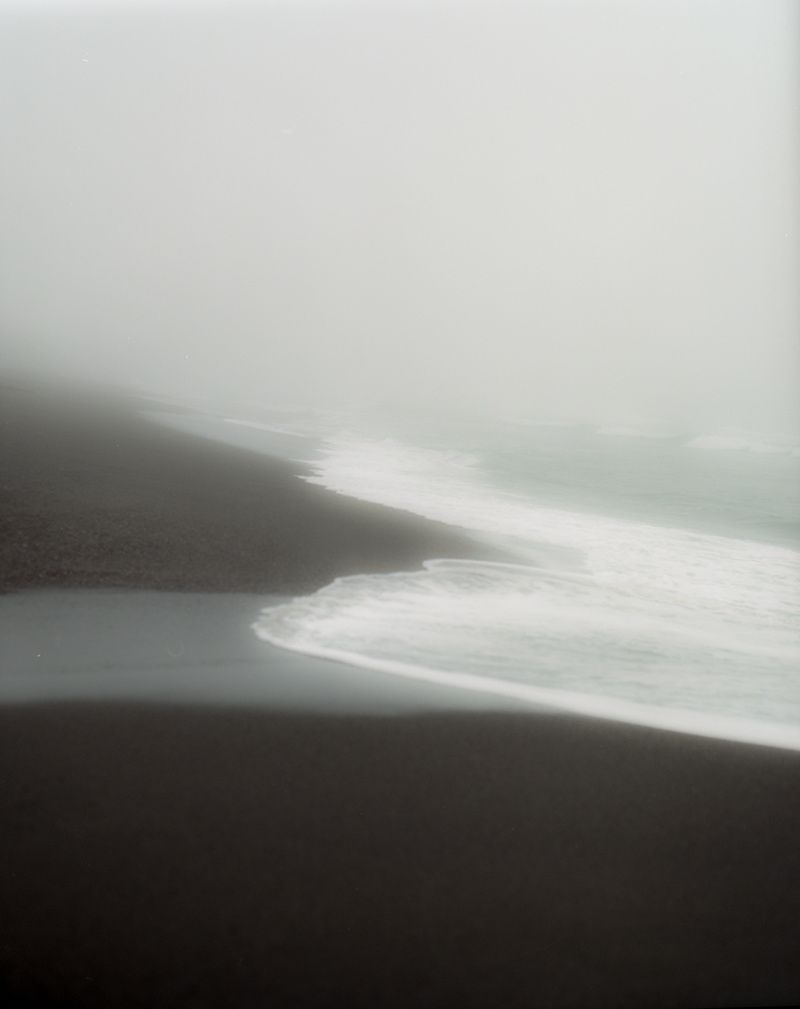 White surf washing onto a dark sand beach that fades into thick fog