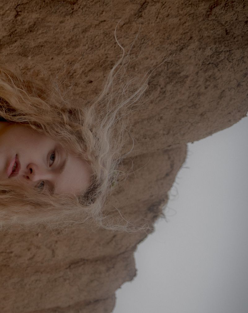 Sideways close-up of a model's face and windswept curly hair against a sandstone rock face